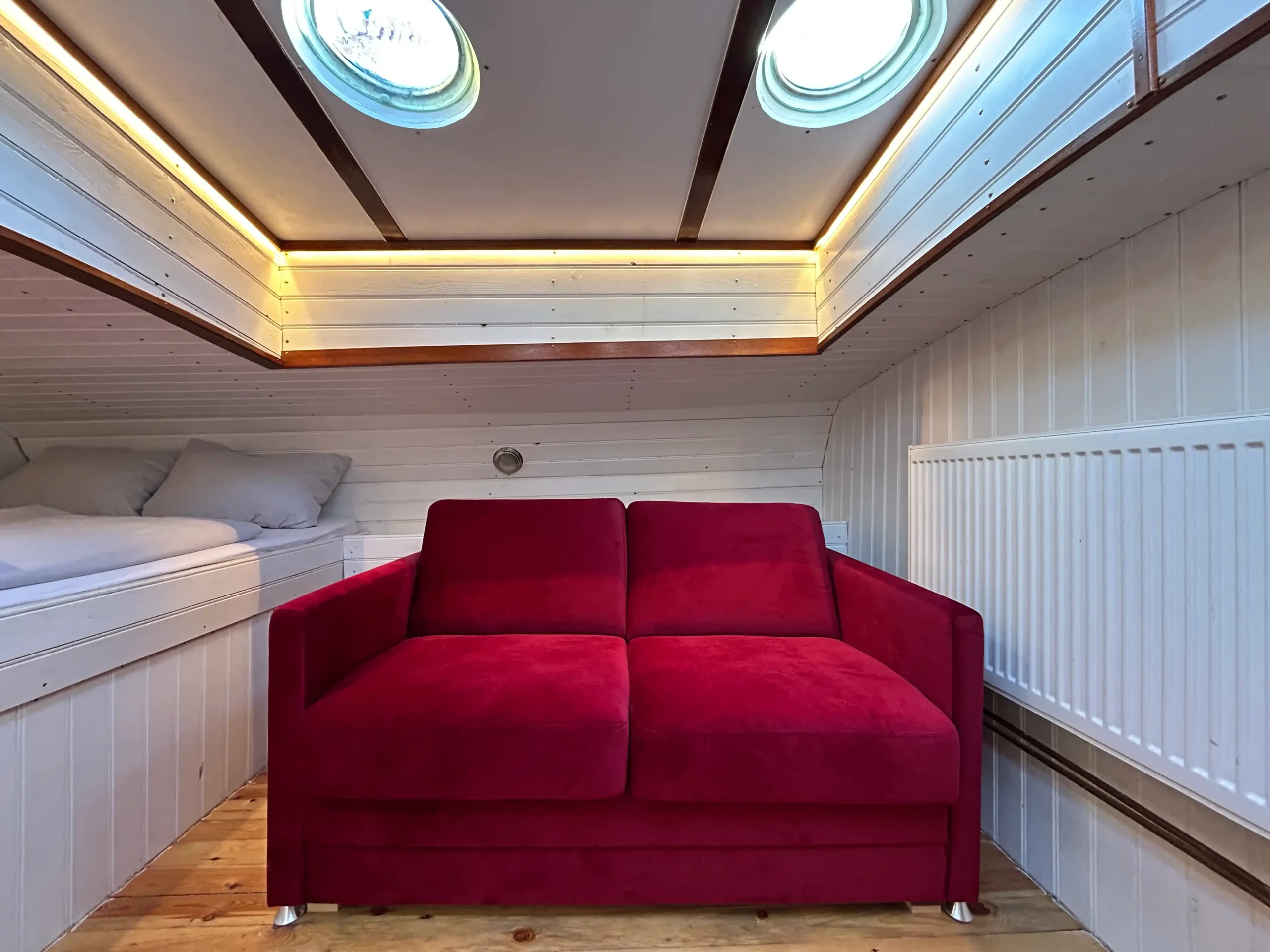 Ein Schlafsofa in roter Samtoptik steht in der vorderen Kajüte auf dem Hausboot Jonathan in Hamburg-Harburg
